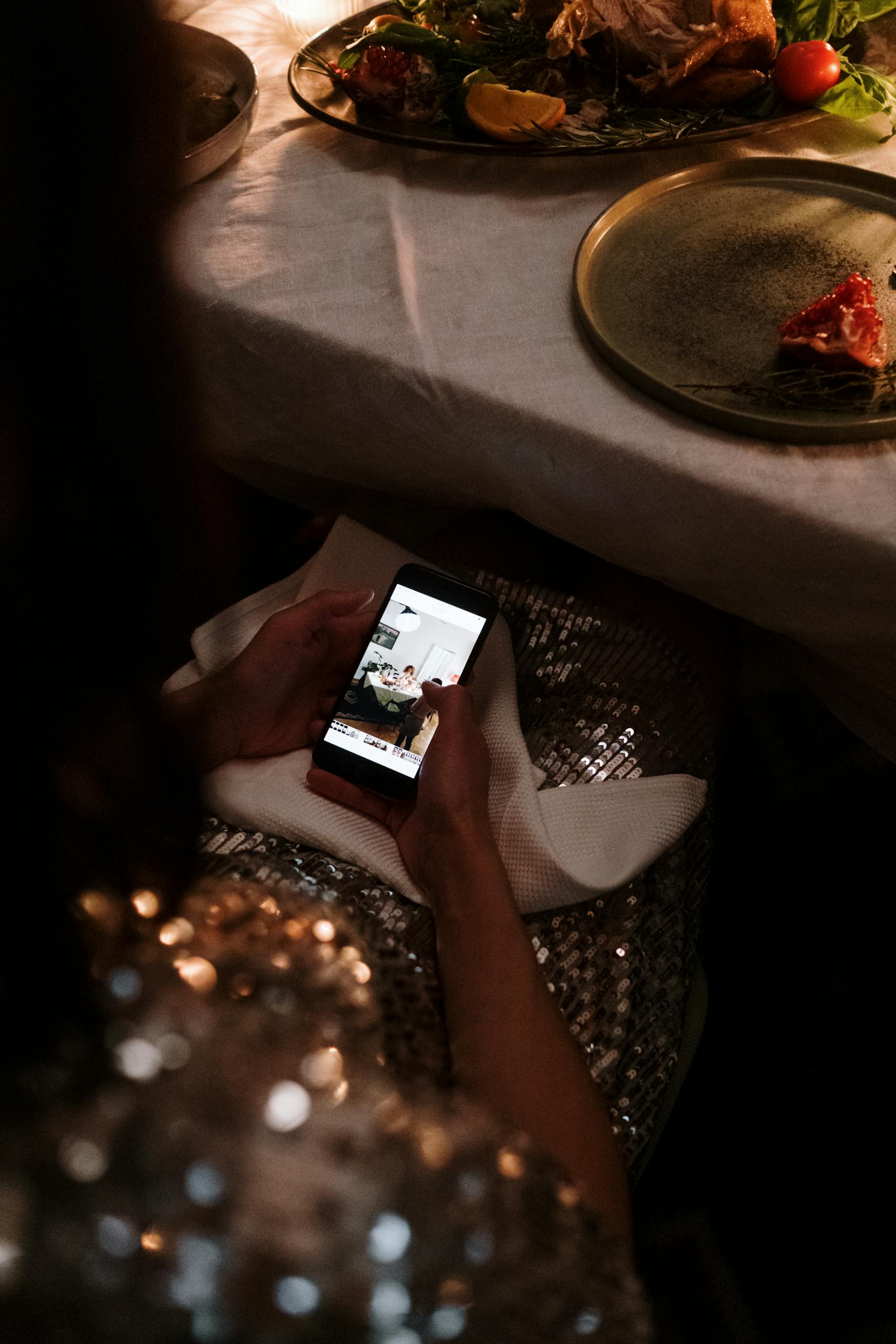 A person in a sequin outfit looks at a smartphone at an elegant dining table.